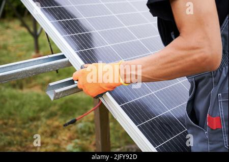Close up of man engineer installing solar modules. Male worker in work gloves mounting solar photovoltaic panel system. Stock Photo