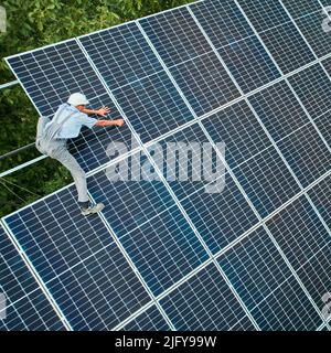 Aerial view of man technician installing photovoltaic solar panels to high steel platform. Concept of alternative energy. Stock Photo