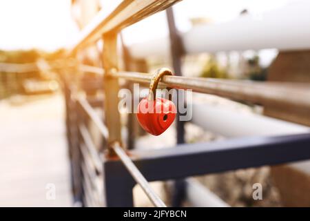 The lock hangs on the metal fence. Symbol of love in the park. The metal red lock in the shape of a heart is locked with a key. A sign of strong love Stock Photo
