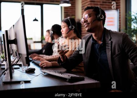 Reception secretary answering client phone call at customer service, helping people at call center support. Male receptionist giving telemarketing assistance on phone helpline in office. Stock Photo