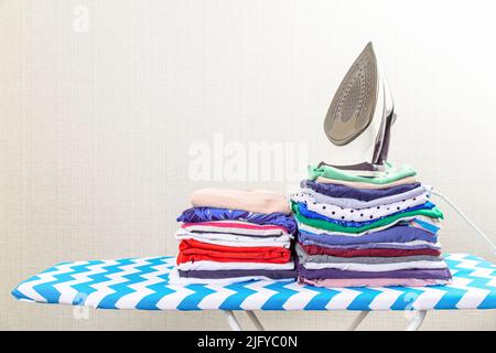 Electric iron and a pile of colorful clothes stacked on an ironing board Stock Photo