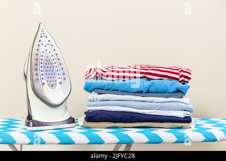 Electric iron and a pile of colorful clothes stacked on an ironing board Stock Photo
