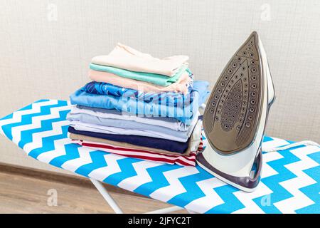 pink electric iron and a stack of ironed clothes on an ironing board on a  white background Stock Photo - Alamy