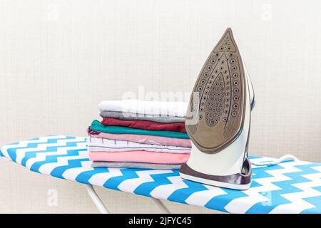 Folded ironed men's shirts lie next to the iron on the ironing board. Stock Photo