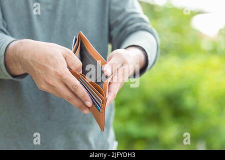 Asian man holding empty wallet. Money problem concept. Outdoor shooting with green blur background Stock Photo