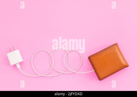 Charging the power to financial concept : Top view white charger cable connect to brown wallet on pink background Stock Photo