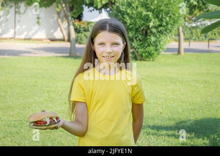 Happy teenage girl eating a burger in the park outdoors. Stock Photo