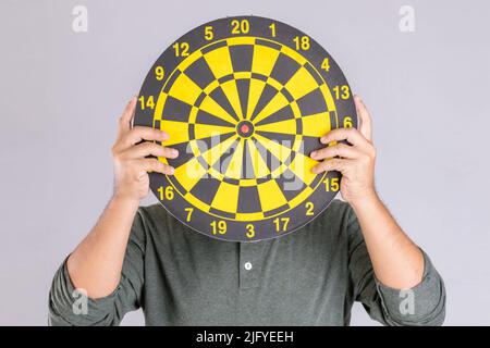 People holding yellow Dartboard and hide his face. Studio shot isolated on grey background Stock Photo