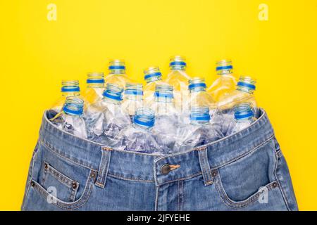 Recycle technology of plastic bottle to make clothes. Top view old water bottle and blue short jeans on yellow background Stock Photo