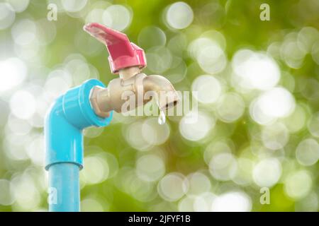 Macro water faucet with one water dripping in garden with green nature bokeh and blur background Stock Photo