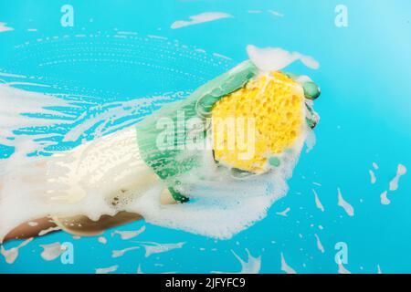 Close up of a hand in rubber gloves wipes the glass with a foam rag. Blue background. The concept of professional cleaning service. Stock Photo