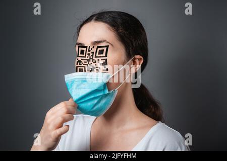 Portrait of a woman with a QR code instead of eyes and nose. Dark background. The concept of chipization and identification about vaccination. Stock Photo
