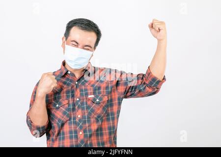 Passed bad situation concept : Asian man wearing protective face mask in action of glad, victory or very happy isolated on grey background Stock Photo