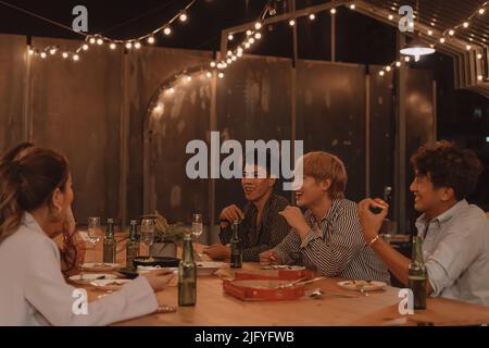 Young Asian friends eating and enjoying dinner together at outdoor restaurant. Friendship and reunion celebration Stock Photo