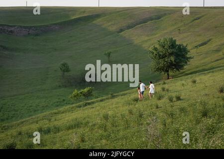 afar view of couple walking with daughter in hilly meadow on summer day Stock Photo