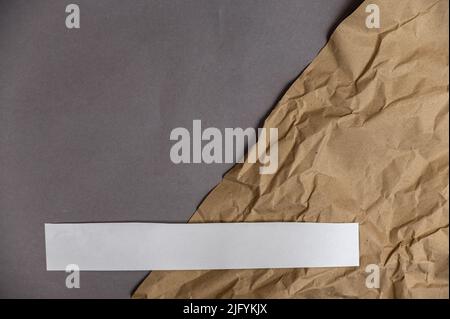 Wrapping paper and a white diagonal stripe against the gray background. Crumpled sheet of light brown paper lies on gray surface. Top view. Space for Stock Photo
