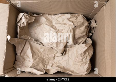 Open cardboard box. Crumpled wrapping paper inside the box. Top view. Selective focus. Stock Photo