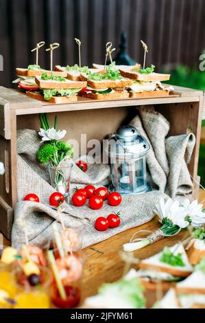 Delicious catering banquet buffet table decorated in rustic style in the garden. Different snacks, sandwiches with ham, chiken, cheese and greenery Stock Photo