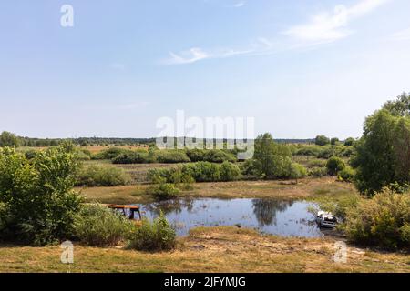 CHERNIHIV REG, UKRAINE - Jun. 19, 2022: War in Ukraine. Burnt and destroyed vehicles, a bus and a passenger car, are abandoned in a small lake. Landscapes of Ukraine after invasion of Russian fascists Stock Photo