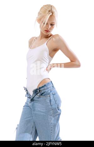 Young tender slender woman wearing oversize jeans posing isolated over white background. Art, beauty, action, flexibility, inspiration concept. Stock Photo