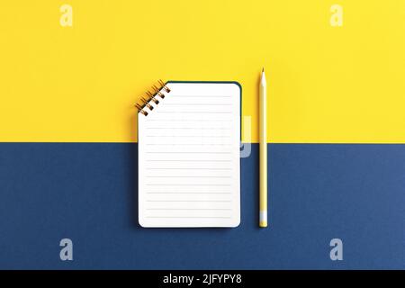 Open spiral notebook with pencil on yellow and blue background. Top view. Stock Photo