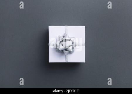 White square gift box with silver bow on grey background, top view. Stock Photo