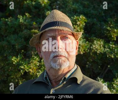 Portrait of an elderly Italian man with straw hat and blue eyes, in a wood Stock Photo