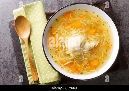 Delicious homemade chicken broth with noodles and vegetables close-up in a plate on a wooden tray. horizontal top view from above Stock Photo