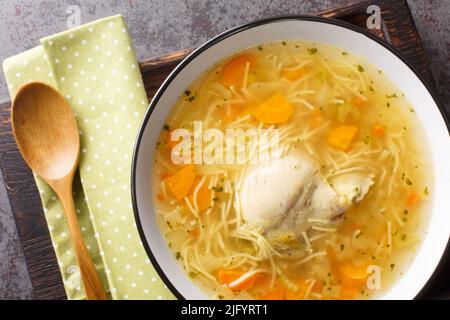 Dietary chicken soup with vermicelli and vegetables close-up in a bowl on a wooden tray on the table. horizontal top view from above Stock Photo