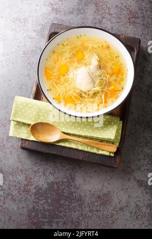 Light chicken soup with pasta and vegetables close-up in a bowl on a wooden tray on the table. Vertical top view from above Stock Photo