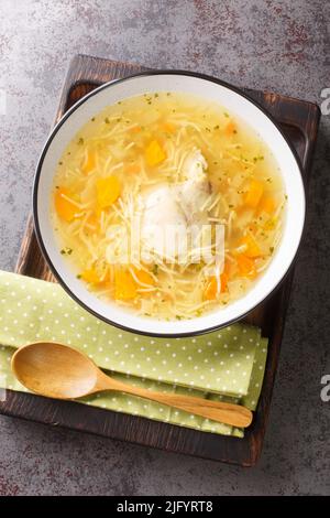Chicken broth with noodles and vegetables close-up in a plate on a wooden tray. Vertical top view from above Stock Photo