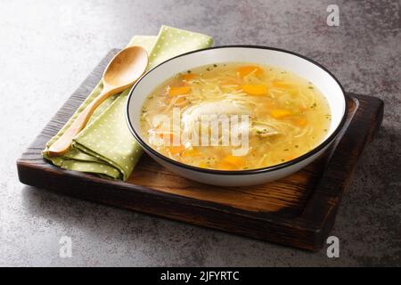 Delicious homemade chicken broth with noodles and vegetables close-up in a plate on a wooden tray. horizontal Stock Photo