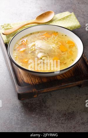 Light chicken soup with pasta and vegetables close-up in a bowl on a wooden tray on the table. Vertical Stock Photo