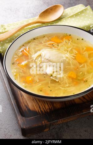 Chicken broth with noodles and vegetables close-up in a plate on a wooden tray. Vertical Stock Photo