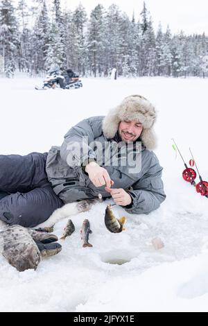 Cheerful man picking up the catch of fish from ice hole, Lapland, Sweden, Scandinavia, Europe Stock Photo