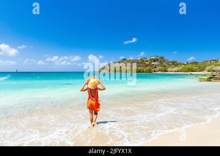 Beautiful woman with orange dress and straw hat standing on a tropical beach, Antigua, West Indies, Caribbean, Central America Stock Photo