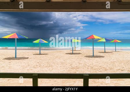 Multicolored striped umbrellas on white sand beach under storm clouds, Antigua, West Indies, Caribbean, Central America Stock Photo