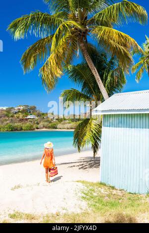 Tourist in orange dress walking on palm fringed beach, Antigua, Leeward Islands, West Indies, Caribbean, Central America Stock Photo