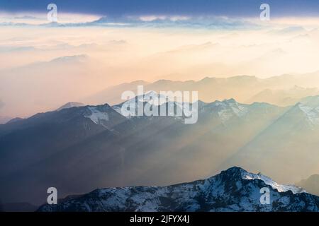 Flying over the snowcapped peaks of Lepontine and Ticino Alps lit by sun rays in the romantic sky at sunset, Switzerland, Europe Stock Photo