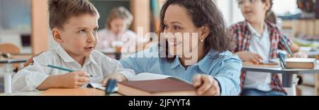 Happy kind teacher is helping a boy in elementary school lessons Stock Photo