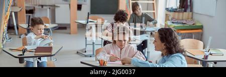 Happy kind teacher is helping kids in elementary school lessons Stock Photo