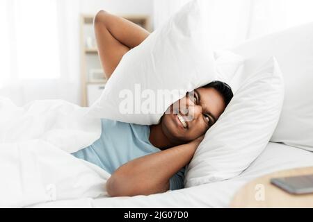 annoyed indian man lying in bed and closing ears Stock Photo
