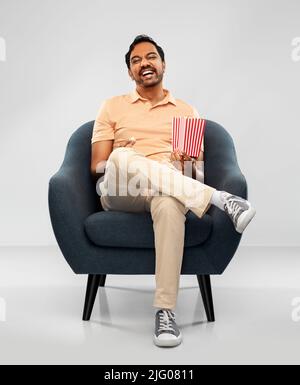 happy smiling indian man eating popcorn in chair Stock Photo