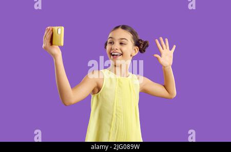 Cheerful trendy kid girl influencer record video vlog and makes selfie on purple background. Stock Photo