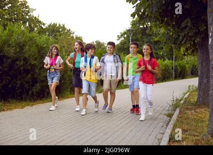 Group of junior high school students with backpacks on their shoulders walk on sidewalk in park. Stock Photo