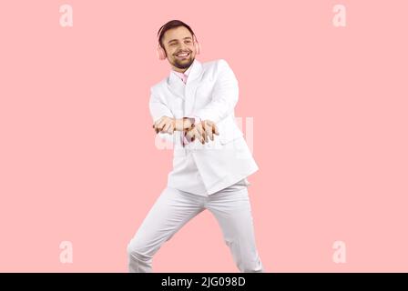 Cheerful man in headphones listens to music and dances in gangnam style on pink background. Stock Photo