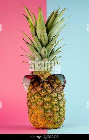 Pineapple with sunglasses. Summer vacation concept on pink and blue background Stock Photo