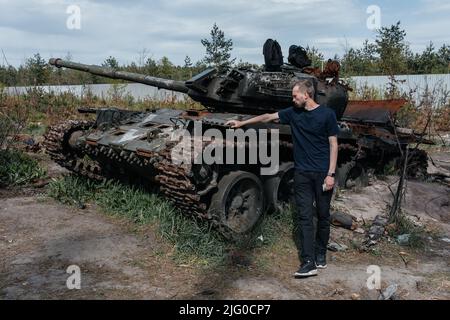 Man stands near destroyed and burned by the Ukrainian army russian tank near Kyiv. Russian military invasion in Ukraine. War in Ukraine and Europe. Stock Photo