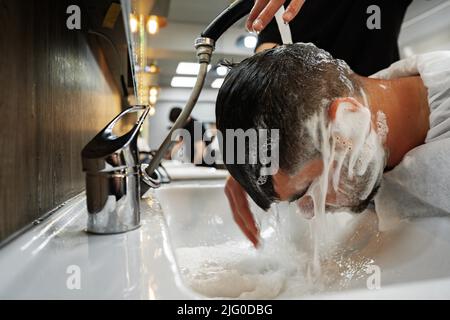 Hairdresser man washes client head in barbershop, close up Stock Photo