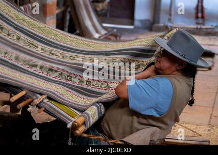 Ecuador, Quito, Paguche. Tahuantinsuyo Weaving Workshop. Traditional "back strap" weaving demonstration. Weaver in typical local attire. Stock Photo